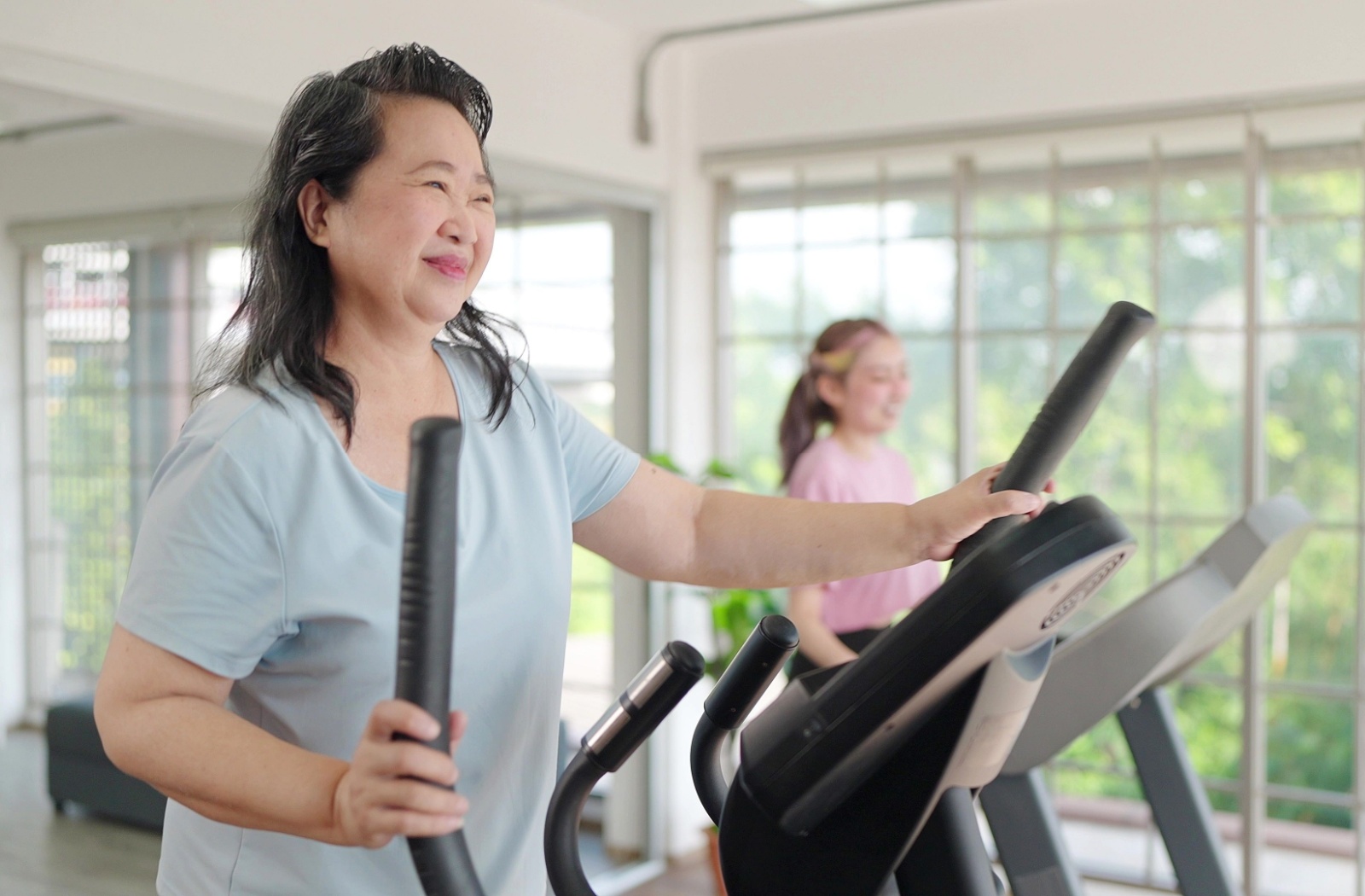 An older adult smiling while exercising on a stationary bike indoors.