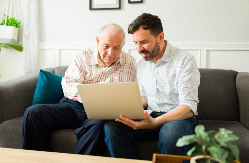 An adult child sits with their parent and helps them set up their Facebook account using a laptop.