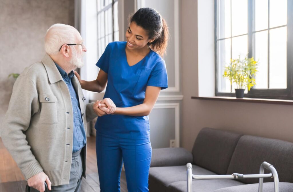A caregiver helping an older adult stand in respite care while smiling at one another.