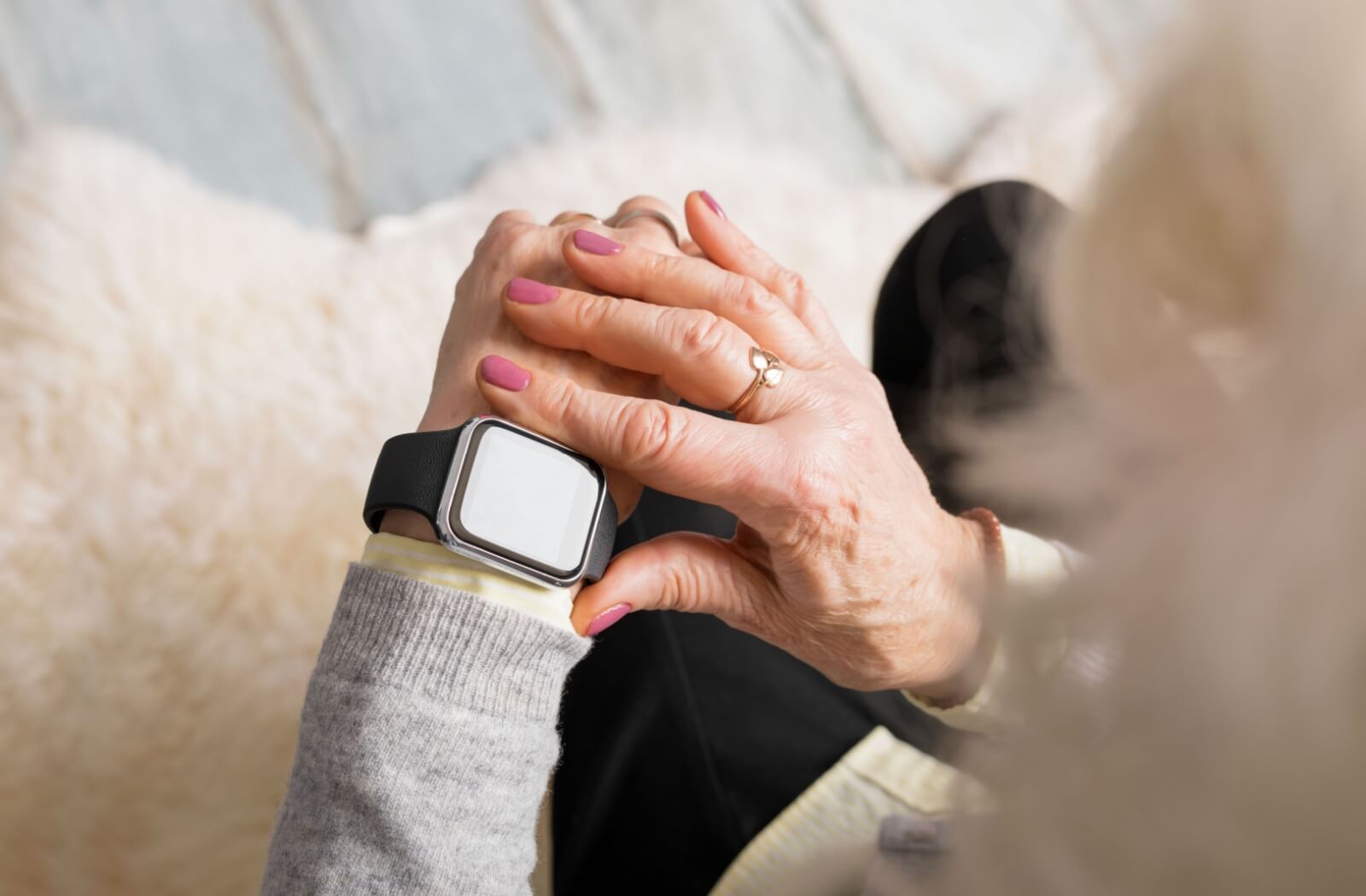 An older adult sits on their couch and adjusts the settings on their smart watch in the morning